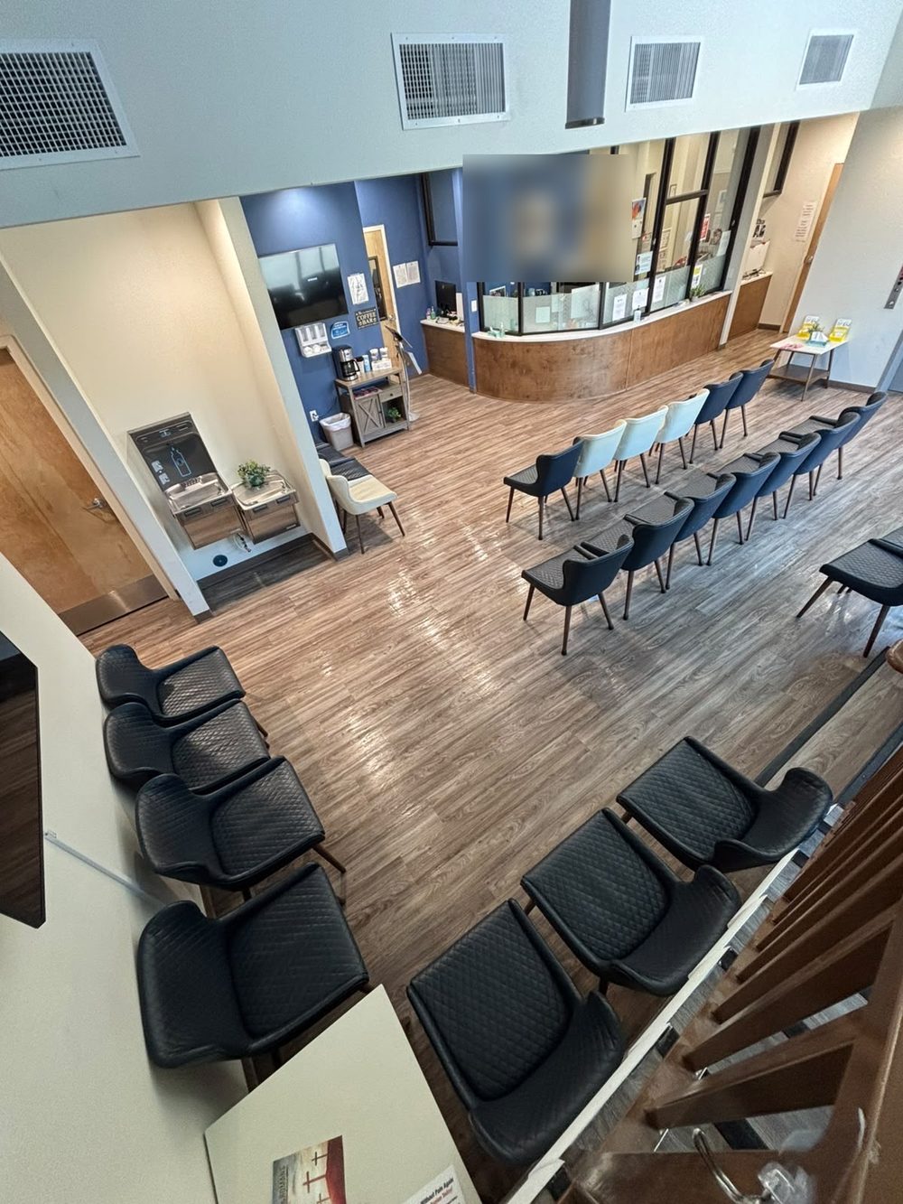 Clinic waiting room and reception desk with rows of chairs and clean flooring, viewed from above